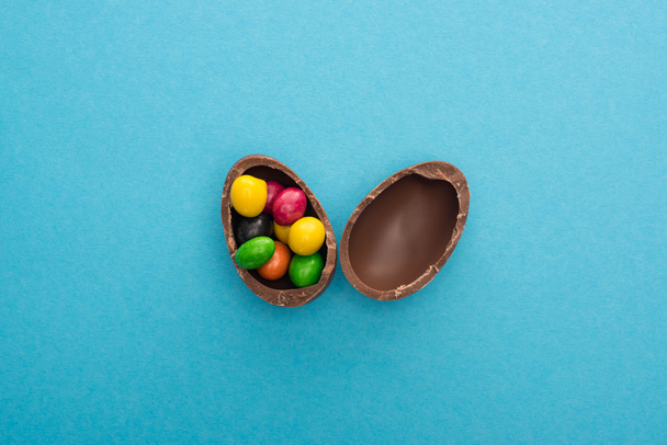 Vista superior de las mitades de huevo de Pascua de chocolate con dulces de colores sobre fondo azul
 - Foto, Imagen
