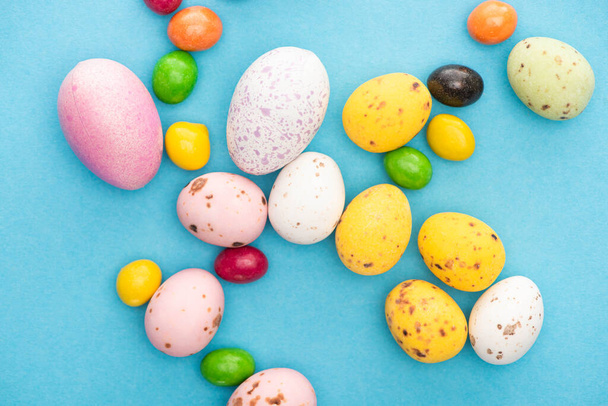 Vista superior de dulces de colores brillantes y huevos de Pascua sobre fondo azul
 - Foto, Imagen