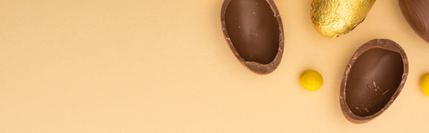 Top view of chocolate eggs with yellow sweets on beige background, panoramic shot - Foto, imagen