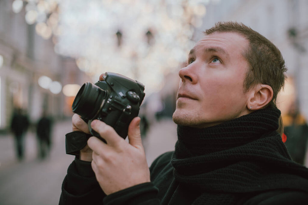 Egy férfi fényképezőgéppel lefényképezi az óvárost télen. Fényképész egy kamera egy kabát és sál a háttérben a mesterien díszített utcai lámpák - Fotó, kép