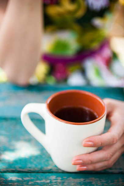 Ahşap masanın üzerinde bir fincan çay tutan bir kadın.. - Fotoğraf, Görsel