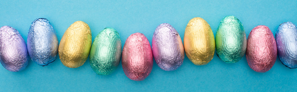 Vue du dessus des œufs de Pâques en chocolat en feuille colorée sur fond bleu, prise de vue panoramique
 - Photo, image