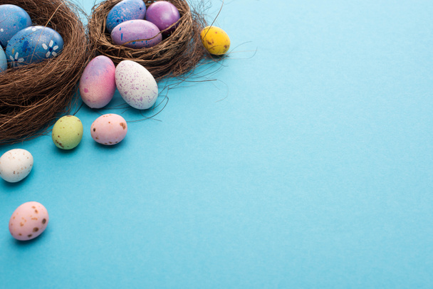 Nests with painted colorful chicken and quail eggs on blue background - Photo, Image