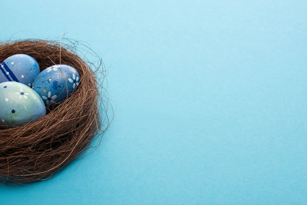Nest with painted chicken eggs on blue background - Foto, imagen