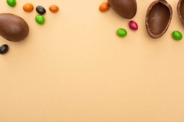 Draufsicht auf Schokoladeneier und bunte Bonbons auf beigem Hintergrund - Foto, Bild