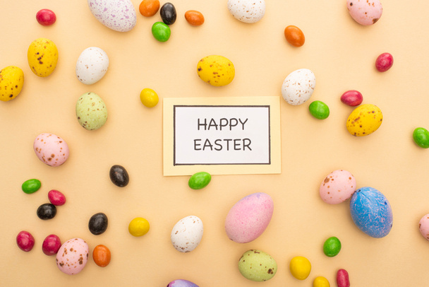 Top view of card with happy easter lettering and bright candies on beige background - Photo, Image