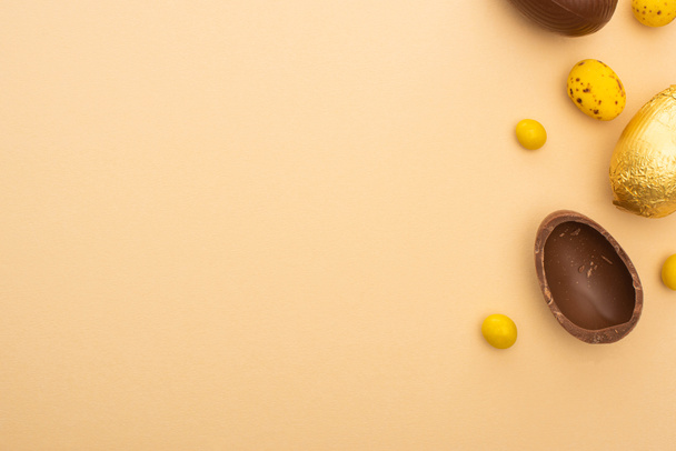 Bovenaanzicht van chocolade Paaseieren met snoepjes en geverfde kwarteleitjes op beige achtergrond - Foto, afbeelding