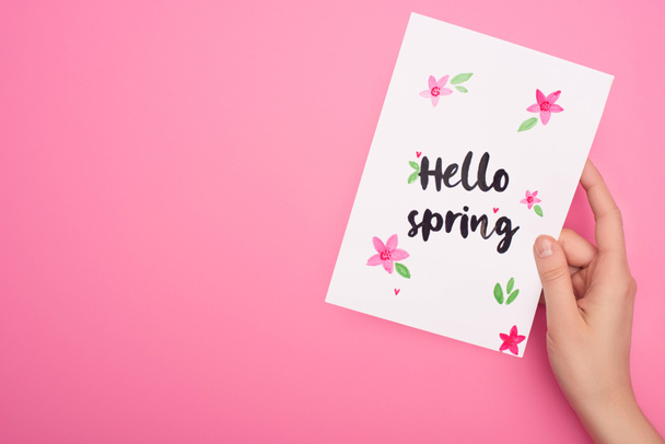 Partial view of card with hello spring lettering in woman hand on pink background - Foto, afbeelding