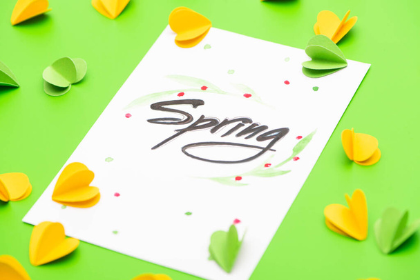 Selective focus of card with spring lettering and decorative hearts on green background - Fotografie, Obrázek