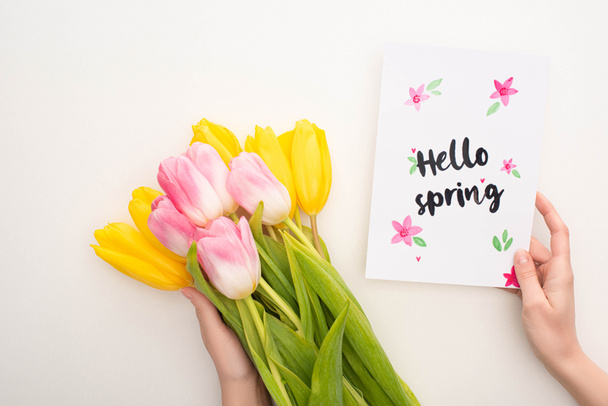 Cropped view of woman holding bouquet of tulips and card with hello spring lettering on white background - Foto, Imagen