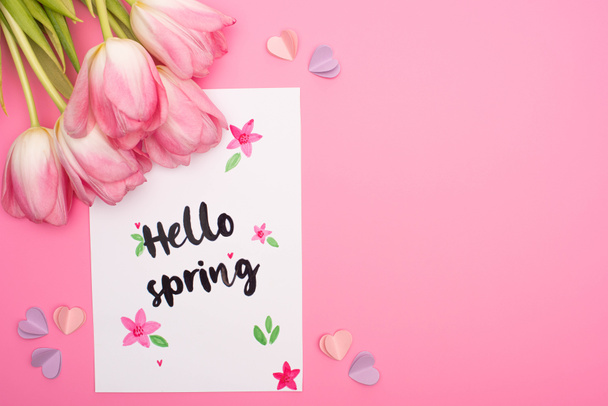 Top view of tulips, card with hello spring lettering and decorative hearts on pink - 写真・画像
