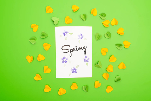 Top view of card with spring lettering with decorative hearts on green background  - Zdjęcie, obraz