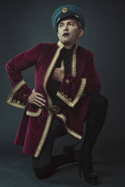 a man portraying a glamorous character in a maroon suede tailcoat and cap - Fotografie, Obrázek
