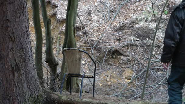 Muž sedí na židli pod stromem v lese a pozoruje okolí - Záběry, video
