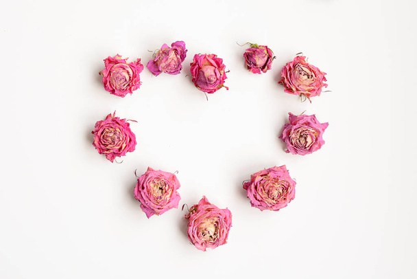 A layout of dry rosebuds in the shape of a heart on a white background. View from above - Zdjęcie, obraz