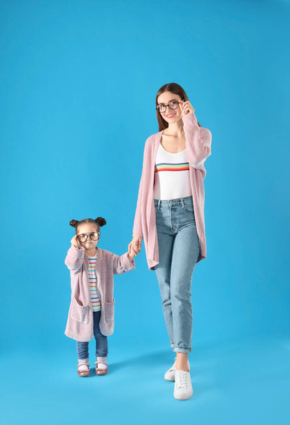 Young mother and little daughter with glasses on blue background - 写真・画像