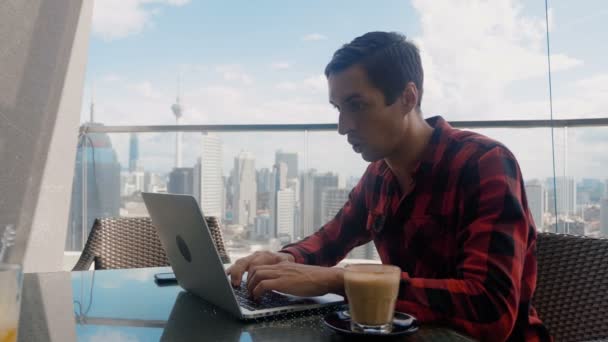 Happy Handsome Man Working on a Laptop Celebrates Successful Endeavor with YES Gesture. Freelancer Working from Cafe on Background of Big City Skyscrapers. - Záběry, video