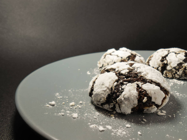 Σπιτικά μπισκότα σοκολάτας. Μπισκότα σοκολάτας σε σκόνη ζάχαρης σε μαύρο φόντο. Επιλεκτική εστίαση - Φωτογραφία, εικόνα