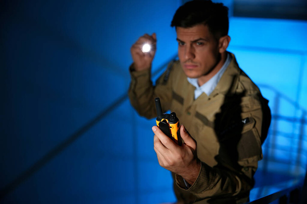 Professional security guard with portable radio set in dark room, focus on hand - Фото, изображение