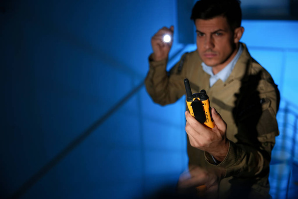 Professional security guard with portable radio set in dark room, focus on hand - Foto, imagen