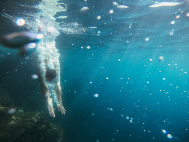 A tenger. A fickó leugrik egy szikláról a tengerbe, és úszik a víz alatt.. - Fotó, kép