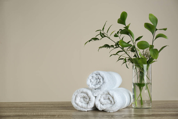 Clean rolled towels and vase with green plants on wooden table. Space for text - Photo, image