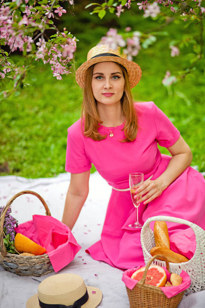 ein Mädchen in einem blühenden Garten auf einem Picknick liegt auf einer Decke mit einem Glas Champagner - Foto, Bild