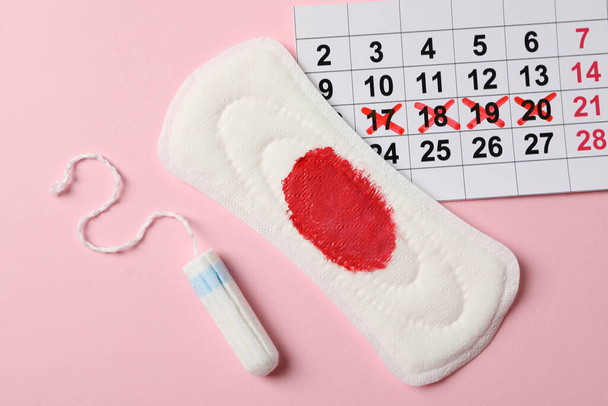 Tampón, almohadilla sanitaria usada y calendario sobre fondo rosa, vista superior
 - Foto, Imagen