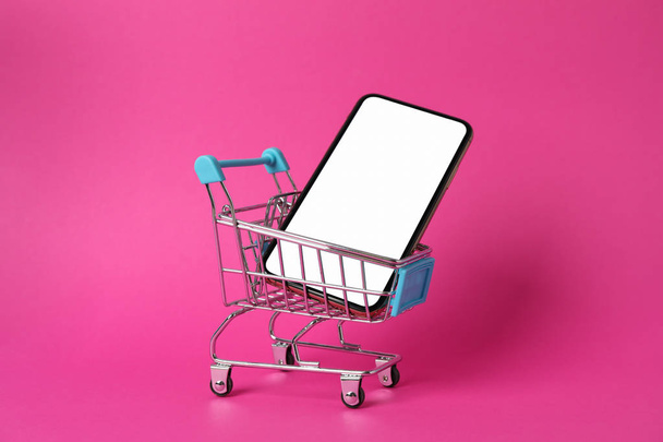 Teléfono con pantalla vacía y carrito de compras sobre fondo rosa, primer plano
 - Foto, imagen