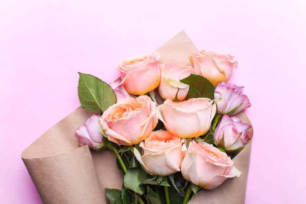 A bouquet of hybrid tea roses and floribunda in craft paper on a pink background. - Zdjęcie, obraz