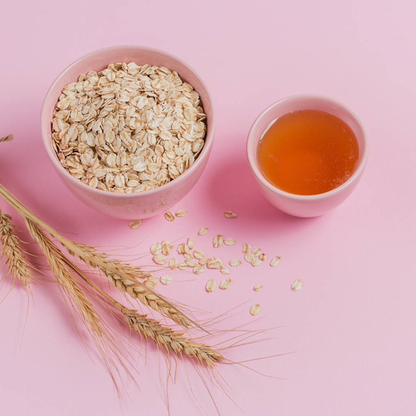 Bowl of dry oat flakes with honey and ears of wheat on light background. Healthy skin, facial and body care. SPA and sauna concept. Top view - Photo, image
