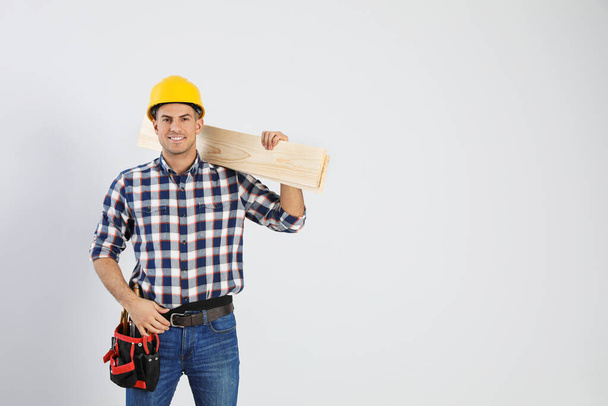 Handsome carpenter with wooden planks on light background. Space for text - Φωτογραφία, εικόνα