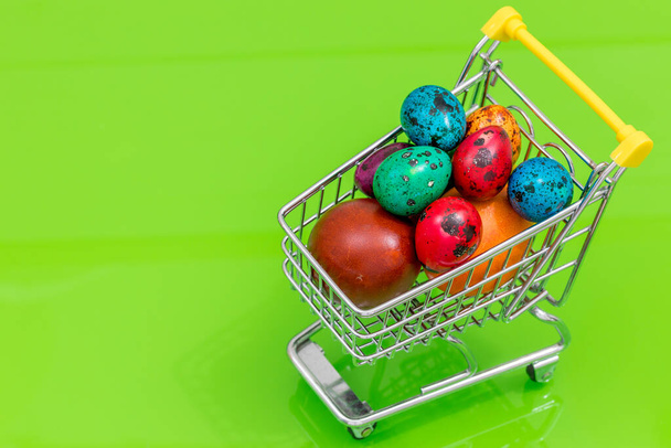 Um carrinho de compras cheio de ovos de Páscoa. O conceito de compras de férias e preços elevados. Fundo verde
,  - Foto, Imagem