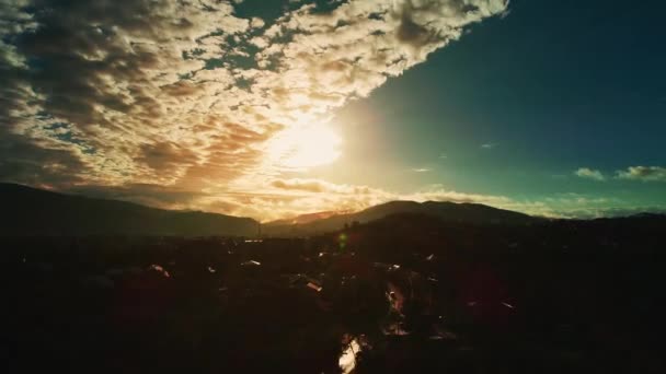 High altitude flight above populated landscape with misty silhouetted mountain range on horizon and view on sunset with fluffy clouds. - Filmmaterial, Video
