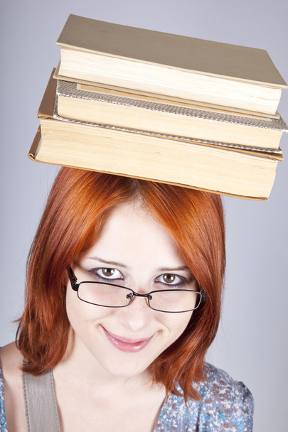 Red-haired girl keep books on her head. Studio shot. - Foto, Imagen