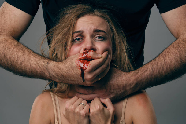Strong man strangling scared female with bruises on her face. Blood from her mouth flows down his arm. Gray background. Domestic violence. Close-up. - Fotoğraf, Görsel