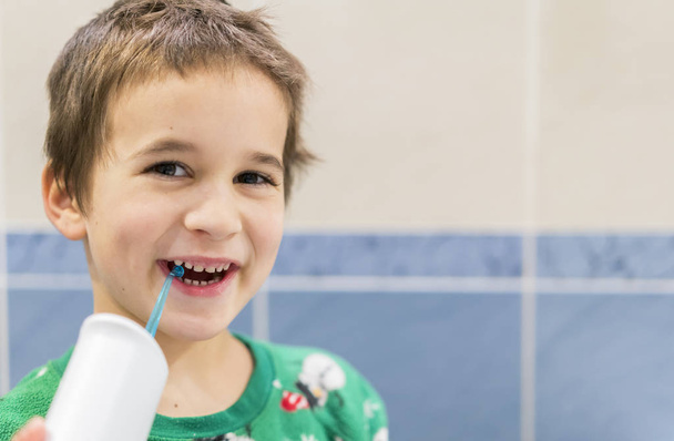 un niño de 5 años de edad en casa se lava los dientes con un irrigador oral. Niño pequeño limpiando dientes con irrigador oral. Concepto de Cuidado Dental. Concepto de cuidado oral
. - Foto, Imagen