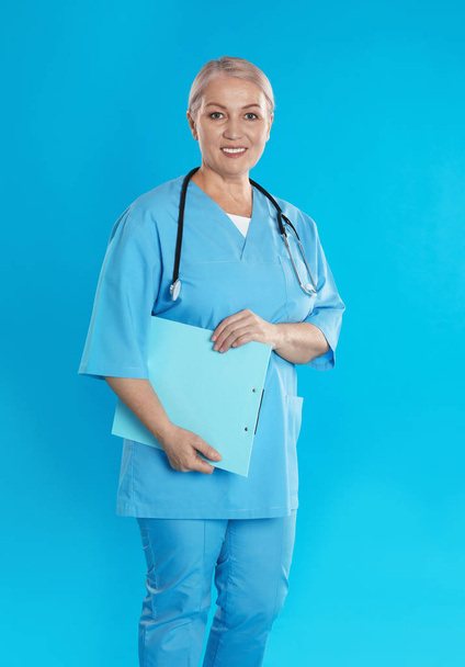 Érett orvos sztetoszkóppal és írótáblával kék alapon - Fotó, kép