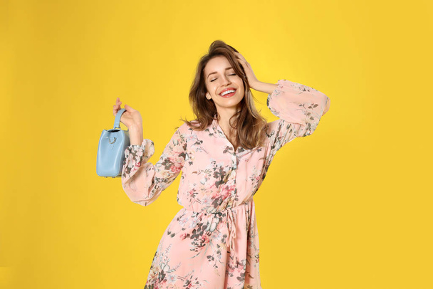 Young woman wearing floral print dress with stylish handbag on yellow background - Foto, Imagen