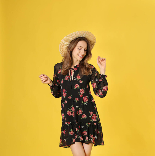 Young woman wearing floral print dress and straw hat on yellow background - Foto, imagen