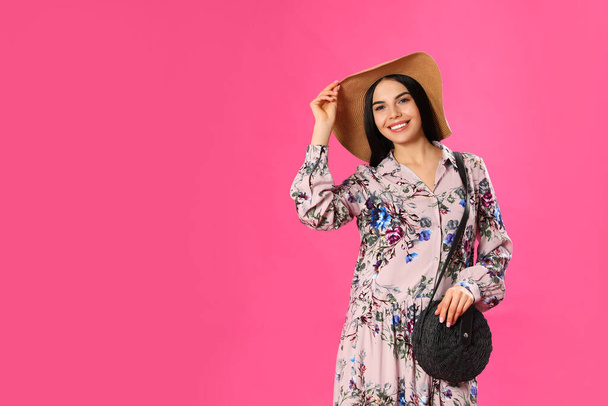 Young woman wearing floral print dress and straw hat on pink background. Space for text - 写真・画像