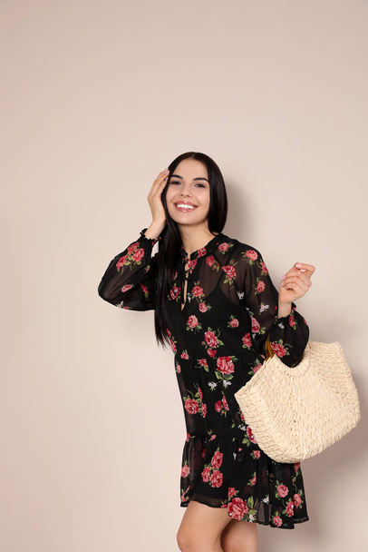 Young woman wearing floral print dress with straw bag on beige background - Foto, Imagem