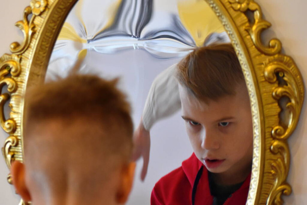 The child reflected in a distorting mirror. A fun reflection of the boy. Children's entertainment - Φωτογραφία, εικόνα