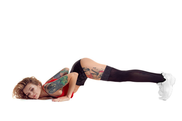 Sexy blonde twerk vrouw met tattoed lichaam en lang krullend haar is poseren in Studio. - Foto, afbeelding