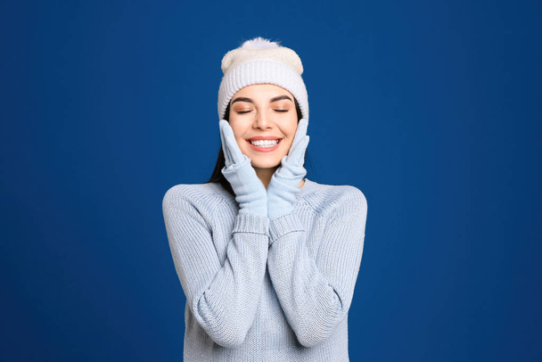 Young woman wearing warm sweater, gloves and hat on blue background. Winter season - Φωτογραφία, εικόνα