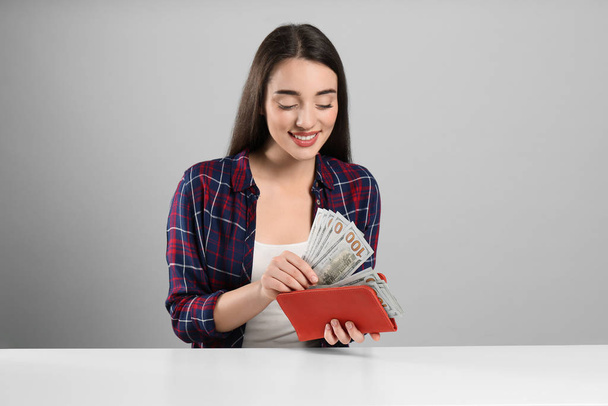 Young woman with money and wallet at table on light grey background - Фото, зображення