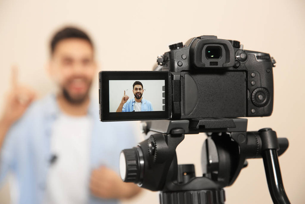 Joven blogger filmando video con cámara contra fondo beige, enfócate en la pantalla
 - Foto, Imagen
