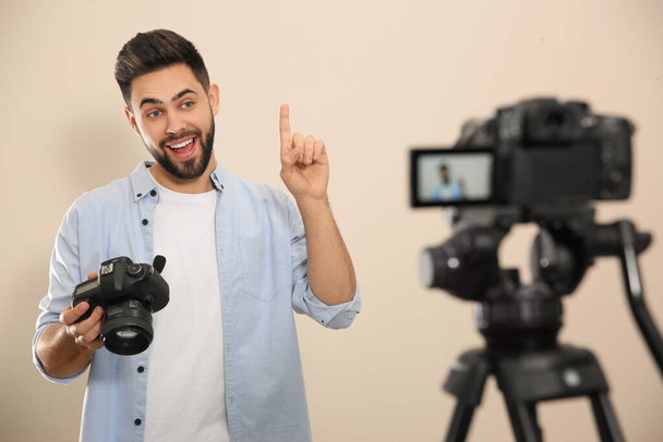 Young blogger with camera recording video against beige background - Zdjęcie, obraz
