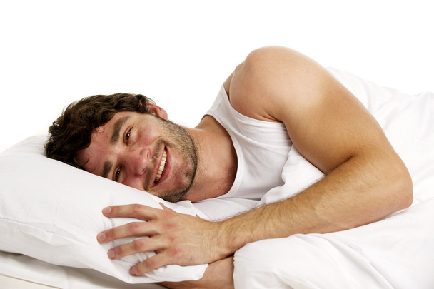 Mies makasi valkoisessa sängyssä hymyillen
 - Valokuva, kuva
