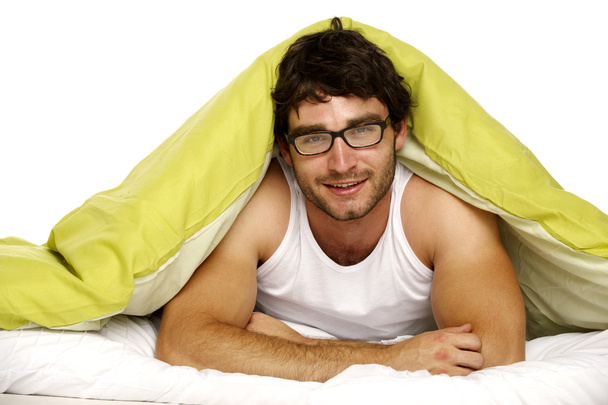άνθρωπος που χαμογελά στο κρεβάτι κάτω από ένα πράσινο πάπλωμα - Φωτογραφία, εικόνα